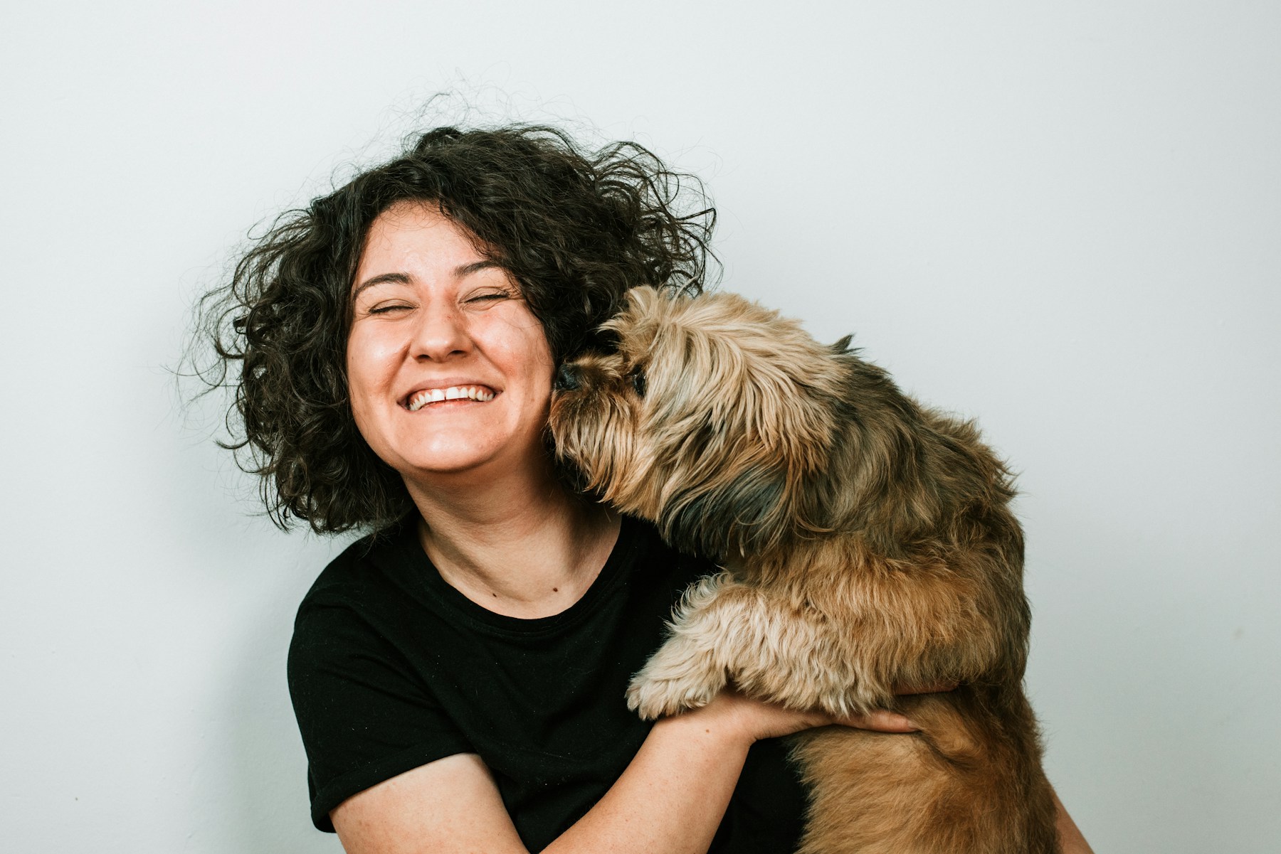 A woman smiling while her dog kisses her cheek